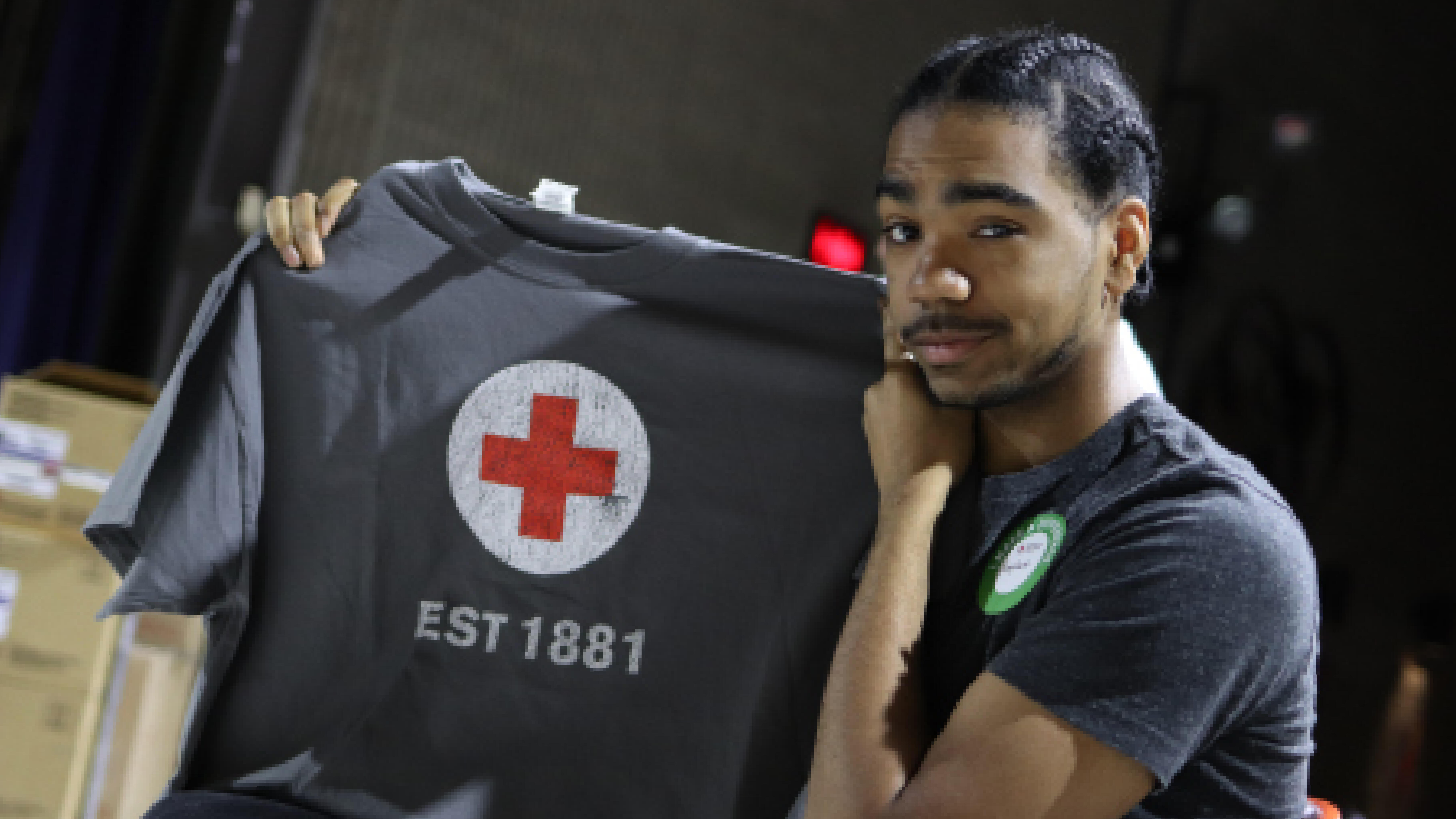 Male student holding up a Red Cross t-shirt after giving blood.