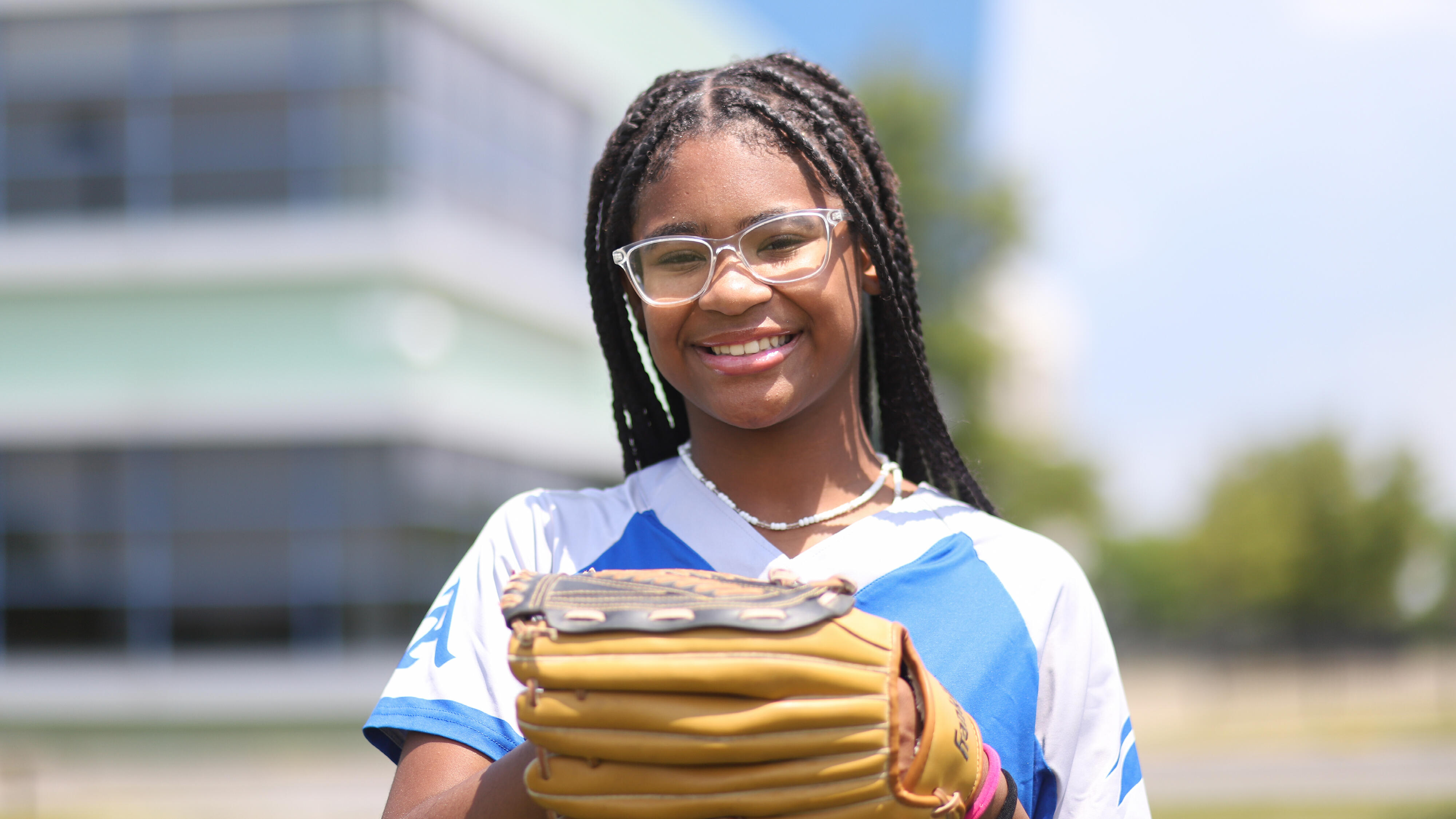 Student wearing a softball uniform and glove and smiling